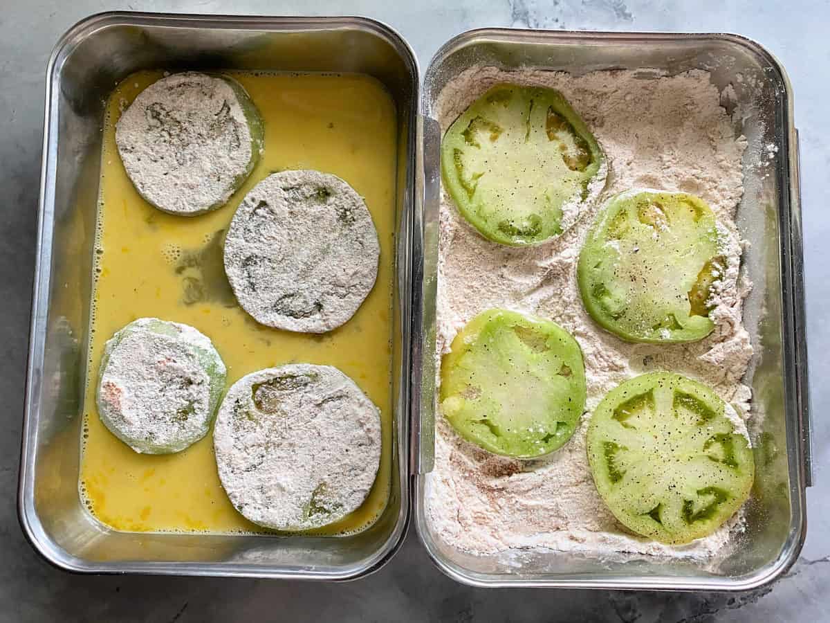 Close up of floured green tomatoes in flour and egg wash tins.