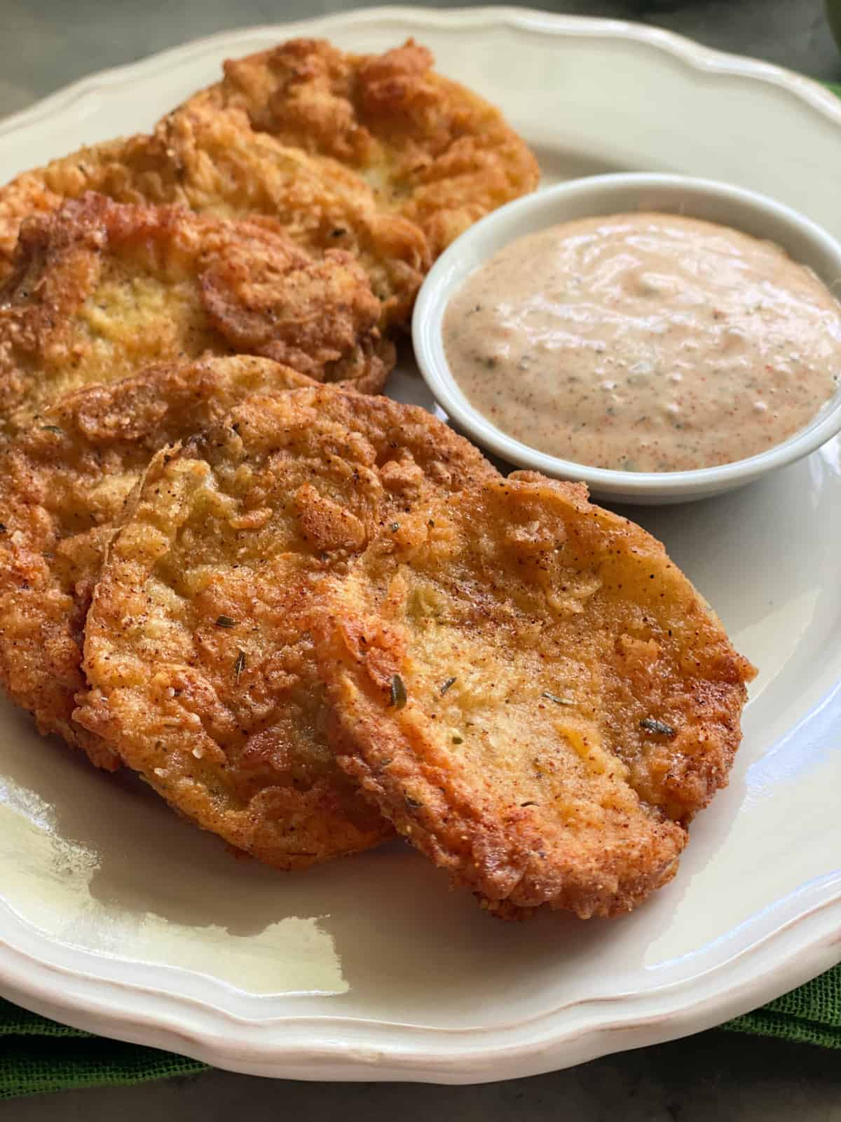 Close up of golden Fried Green Tomatoes on a white plate with ranch dipping sauce.