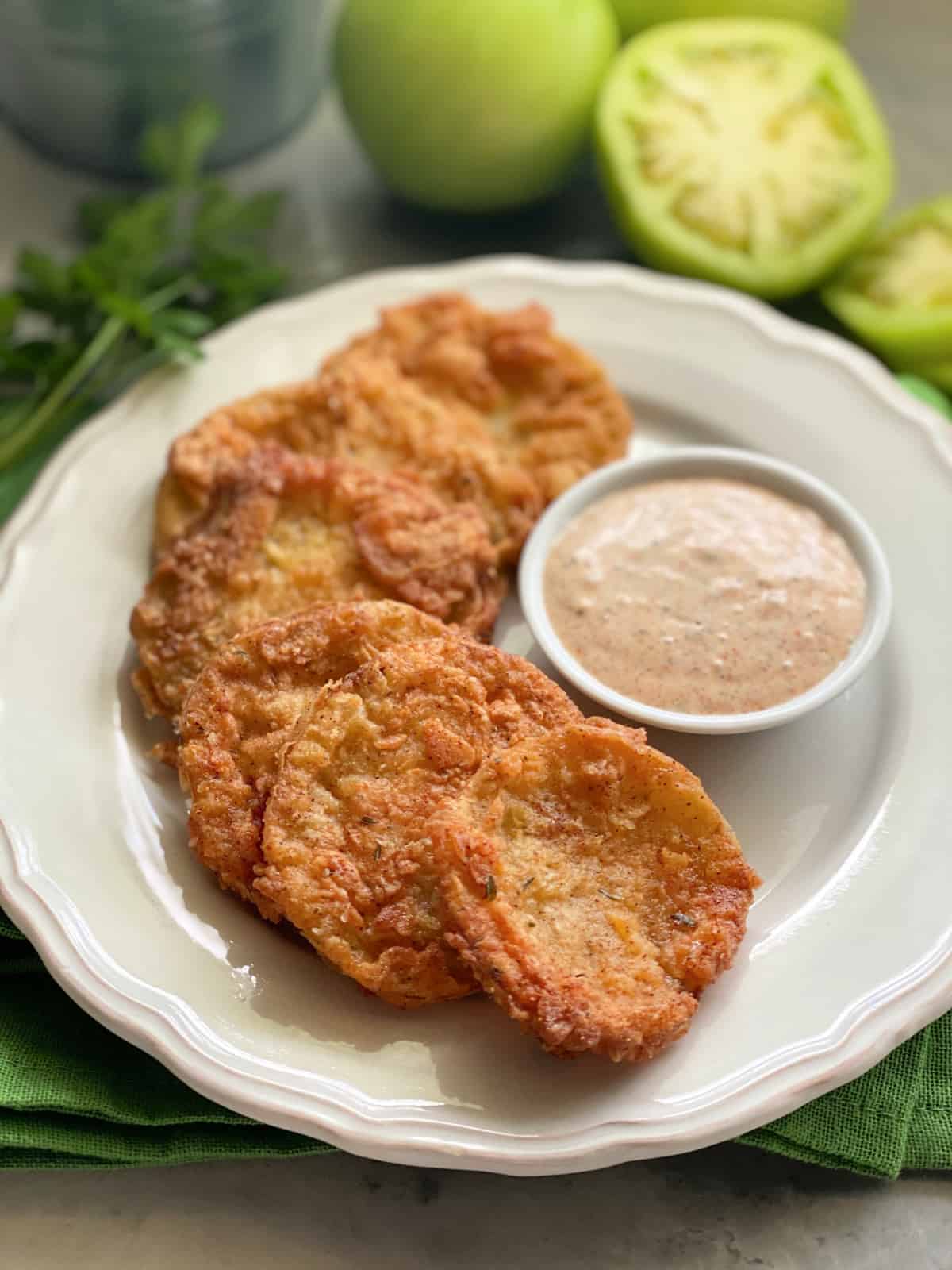 Golden Fried Green Tomatoes stacked on a plate with sauce.