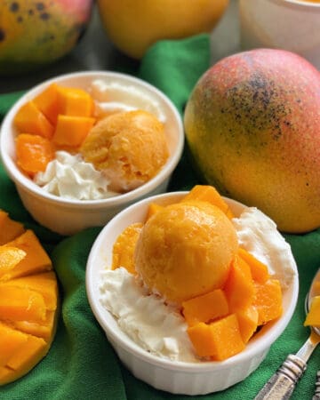 Two white bowls filled with orange frozen yogurt with whipped cream on a dark green cloth.