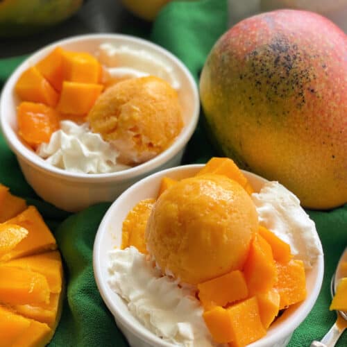 Two white bowls filled with orange frozen yogurt with whipped cream on a dark green cloth.