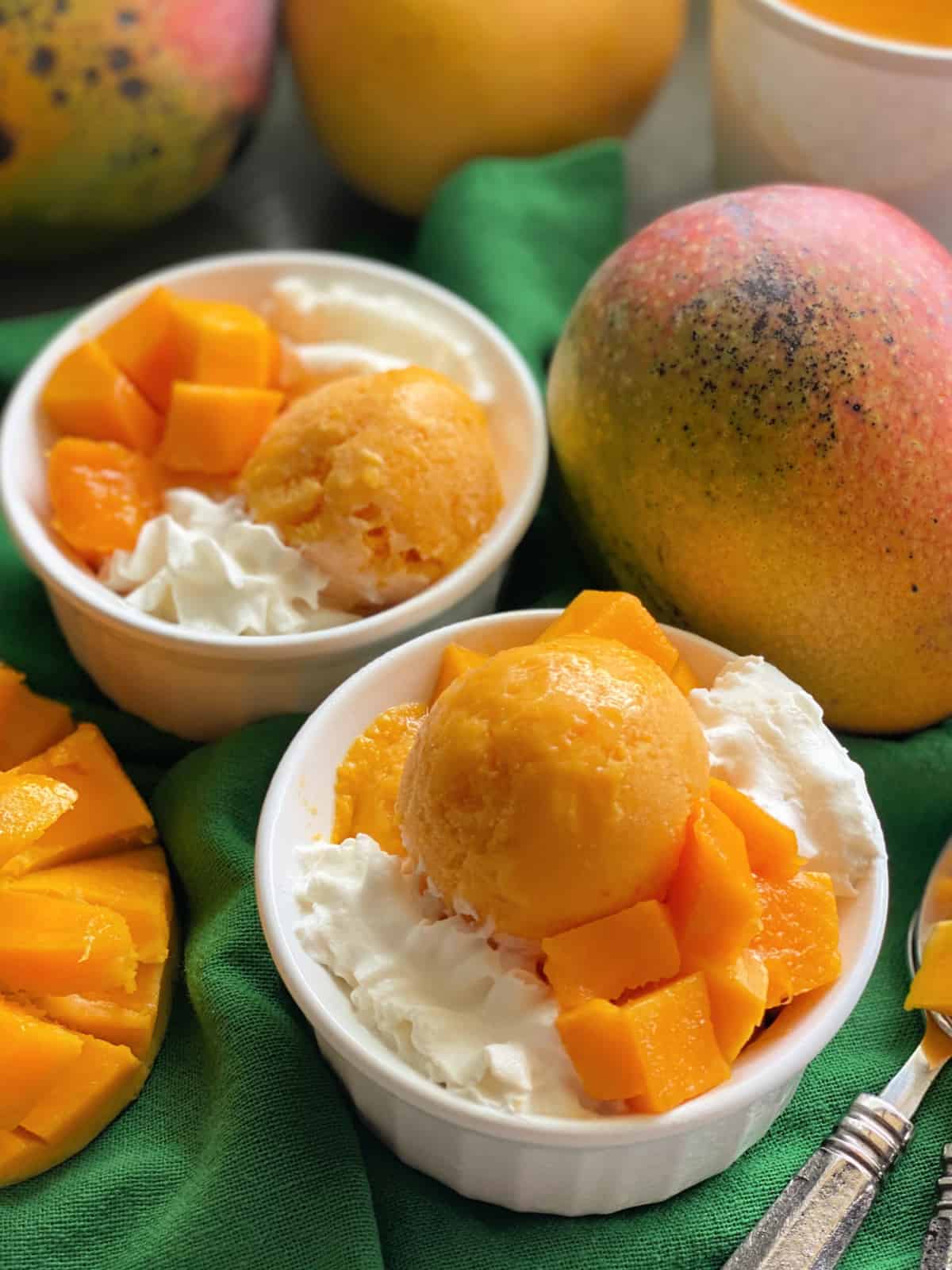 Two white bowls filled with orange frozen yogurt with whipped cream on a dark green cloth.