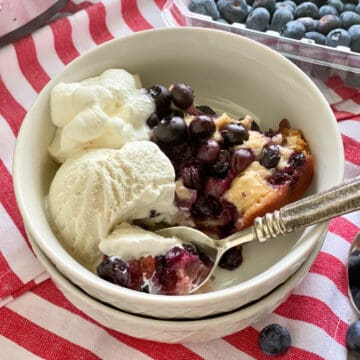 Two white bowls stacked and filled with blueberry cobbler with vanilla ice cream.