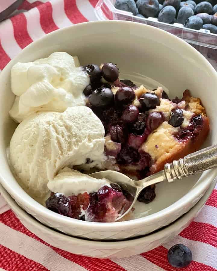 Two white bowls stacked and filled with blueberry cobbler with vanilla ice cream.