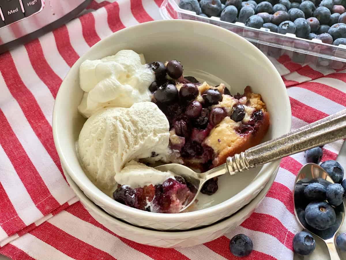 Two white bowls stacked and filled with blueberry cobbler with vanilla ice cream.