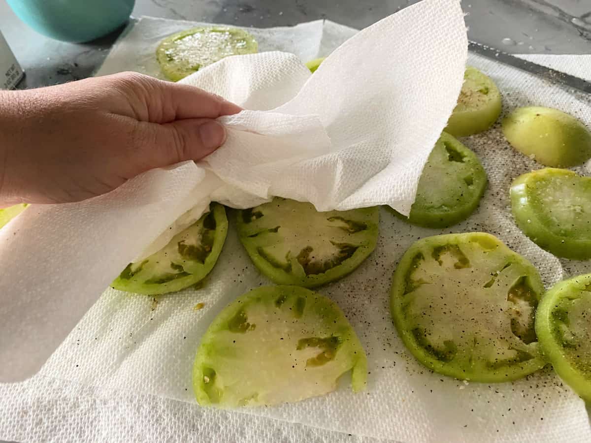 Hand blotting sliced green tomatoes with a paper towel.