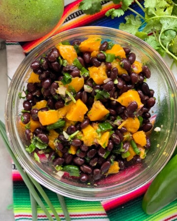 Glass bowl with black beans, mango and green onion with cilantro.