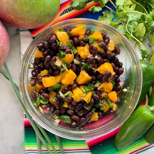 Glass bowl with black beans, mango and green onion with cilantro.