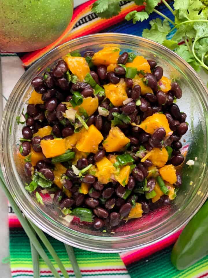 Glass bowl with black beans, mango and green onion with cilantro.