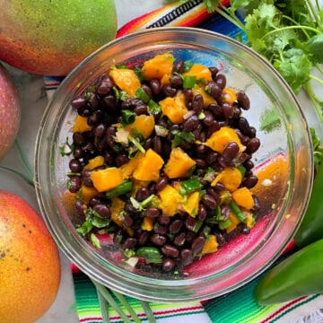 Top view of a bowl filled with black beans and mangoes on top of a kitchen towel with fresh jalapenos and manges.