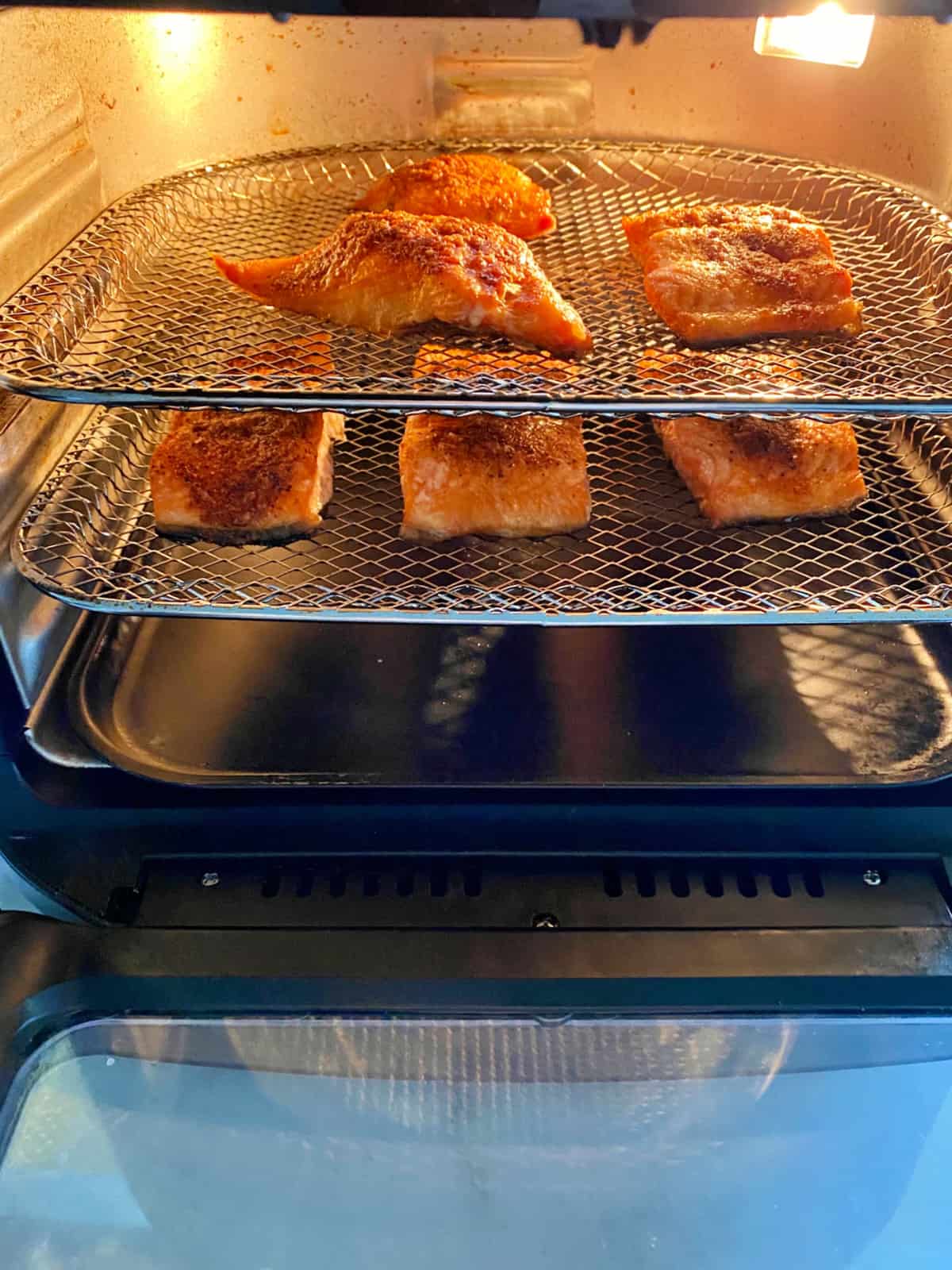 Two mesh trays in an air fryer with salmon filets on trays.
