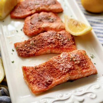 White platter filled with 4 seasoned salmon filets with lemon wedges on platter.