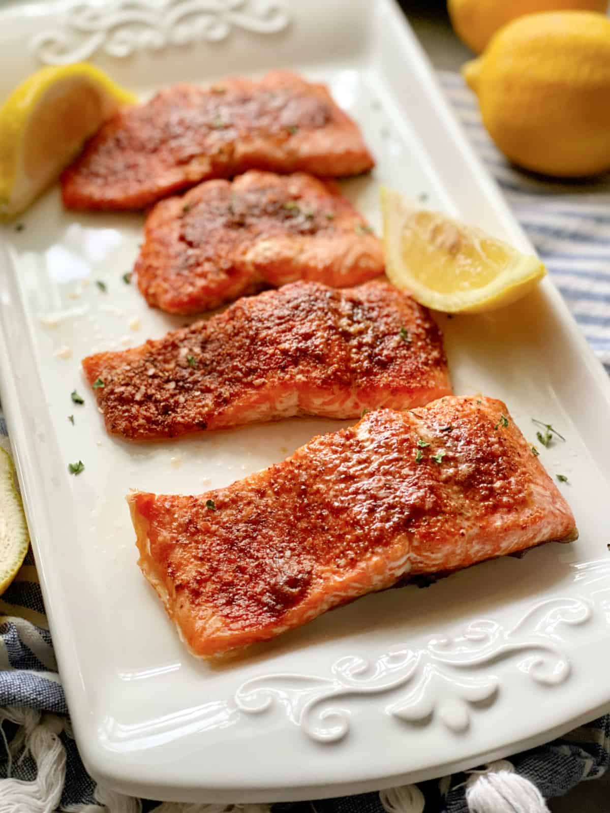 White platter filled with 4 seasoned salmon filets with lemon wedges on platter.