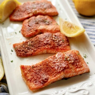 Four salmon filets on a white platter with lemon.