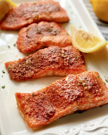 Four salmon filets on a white platter with lemon.