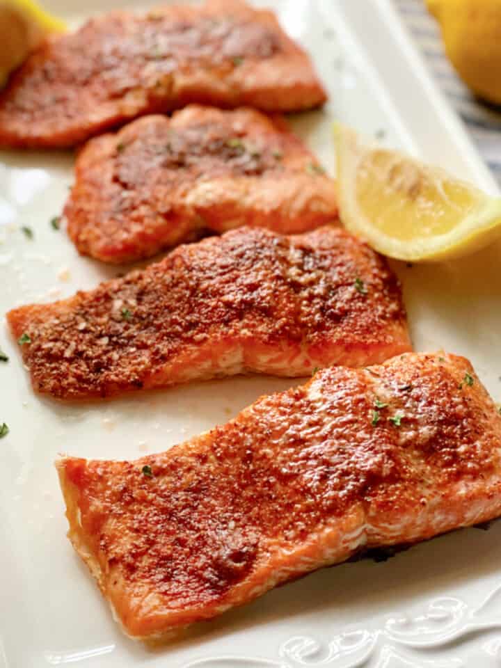 Four salmon filets on a white platter with lemon.