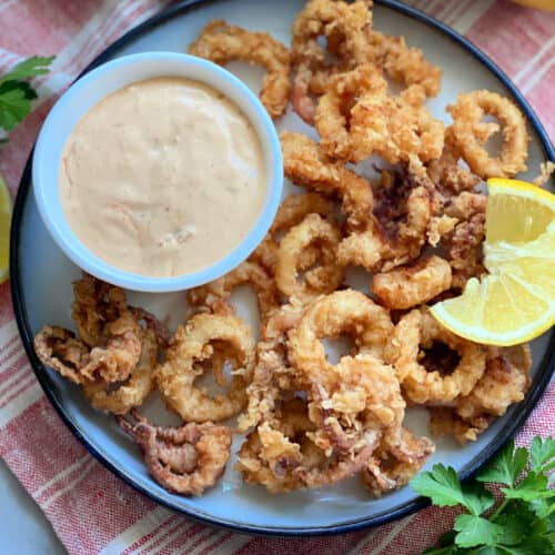 Top view of a white plate filled with lemon wedge, aioli sauce, and fried calamari.