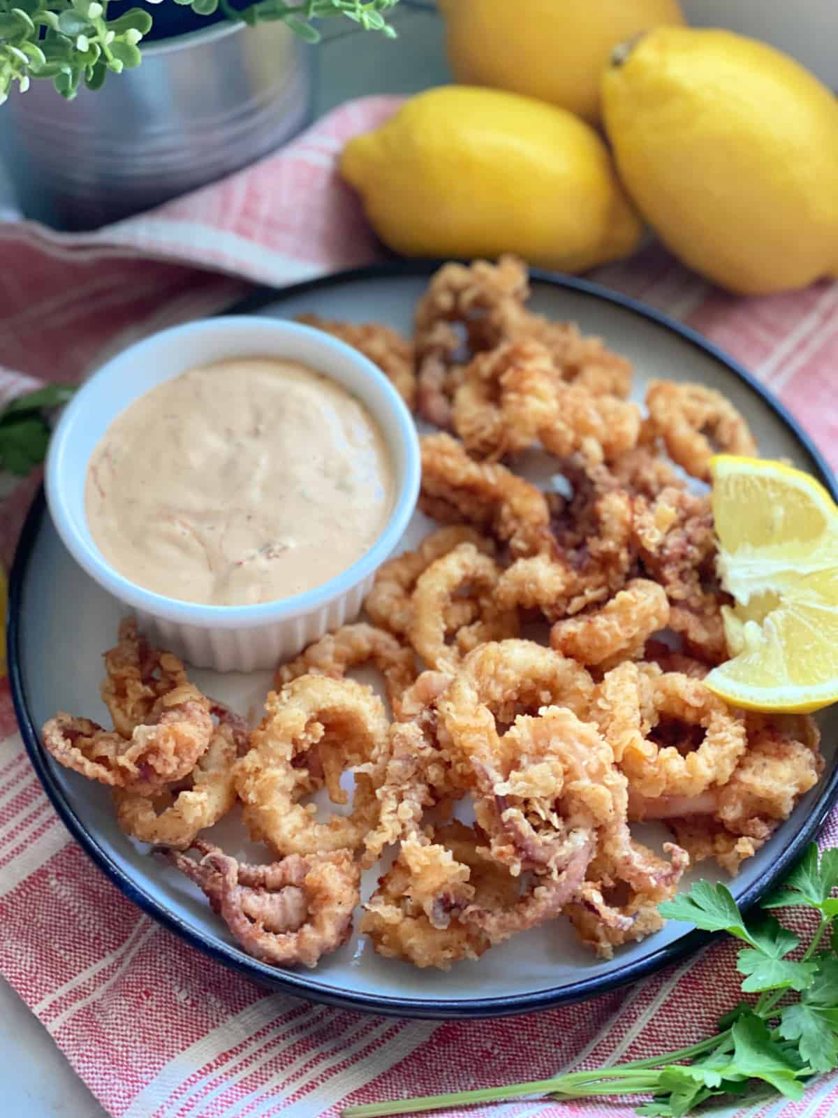 White plate filled with fried calamari with lemon wedge and dipping sauce.