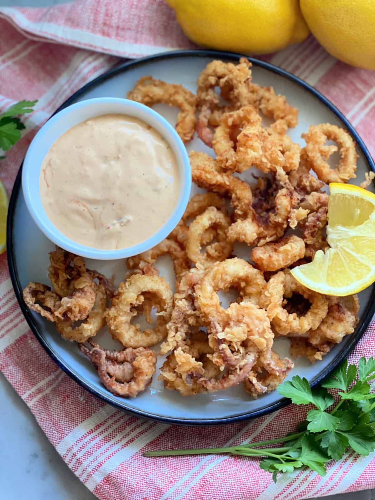 Top view of a white plate filled with lemon wedge, aioli sauce, and fried calamari.