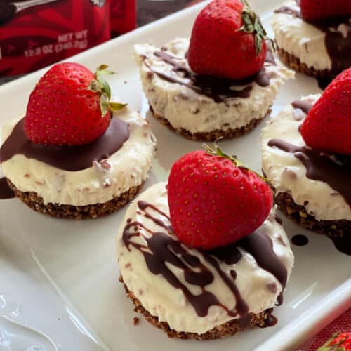 Close up of cheesecake cupcakes with strawberries and melted chocolate drizzled on top.