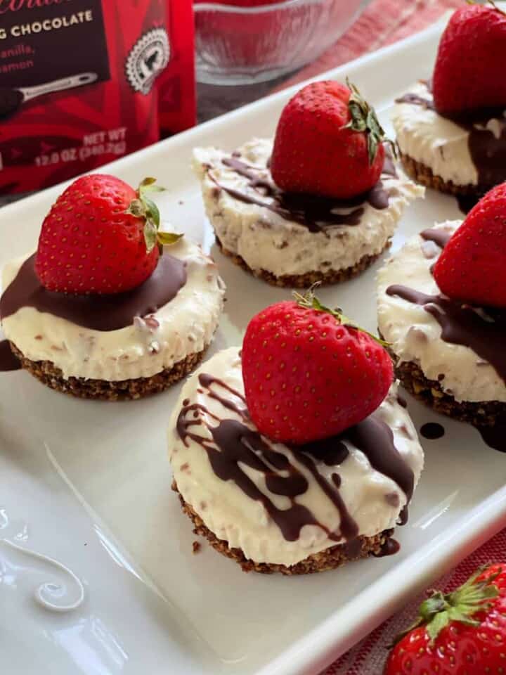 Close up of cheesecake cupcakes with strawberries and melted chocolate drizzled on top.