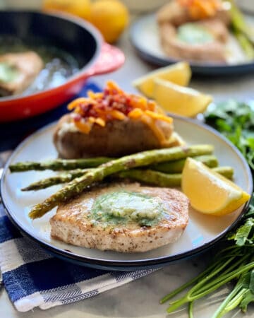 White plate filled with a swordfish steak with butter, asparagus, and a baked potato.