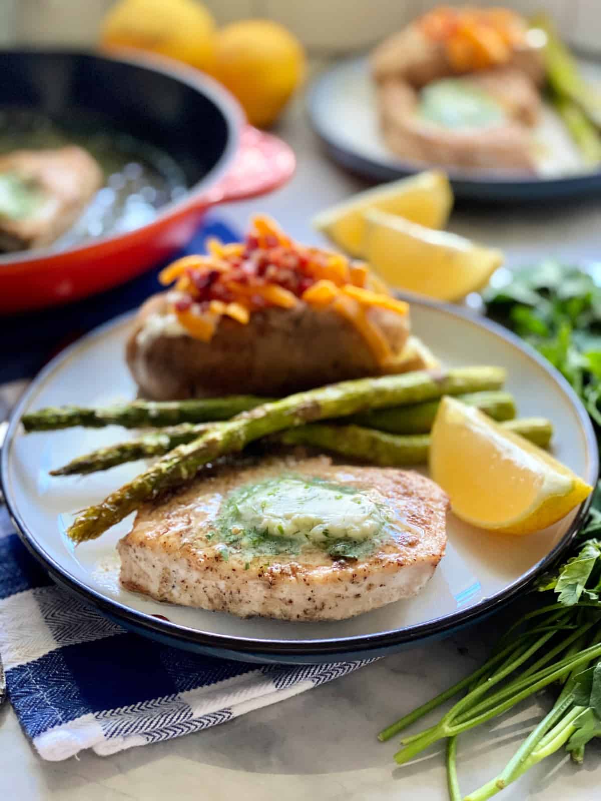 White plate filled with a swordfish steak with butter, asparagus, and a baked potato.