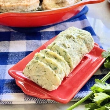 red plate with a log of herb butter sliced on top.