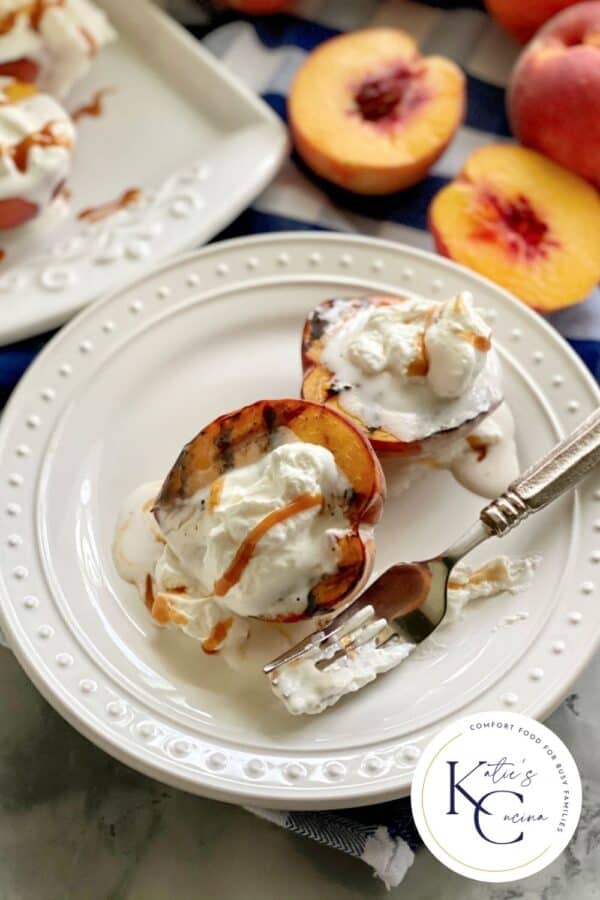 White plate filled with two grilled peaches with a fork and whipped cream with logo on right corner of photo.
