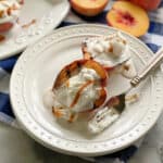 Top view of a white plate filled with two grilled peaches, whipped cream, and caramel sauce.