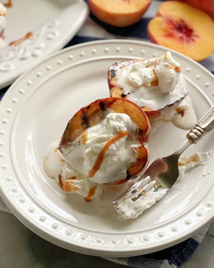 Top view of a white plate filled with two grilled peaches, whipped cream, and caramel sauce.