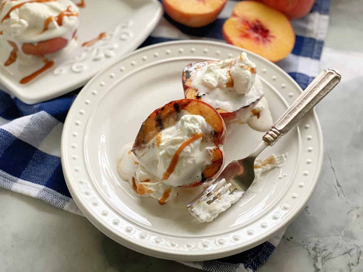 Top view of a white plate filled with two grilled peaches, whipped cream, and caramel sauce.