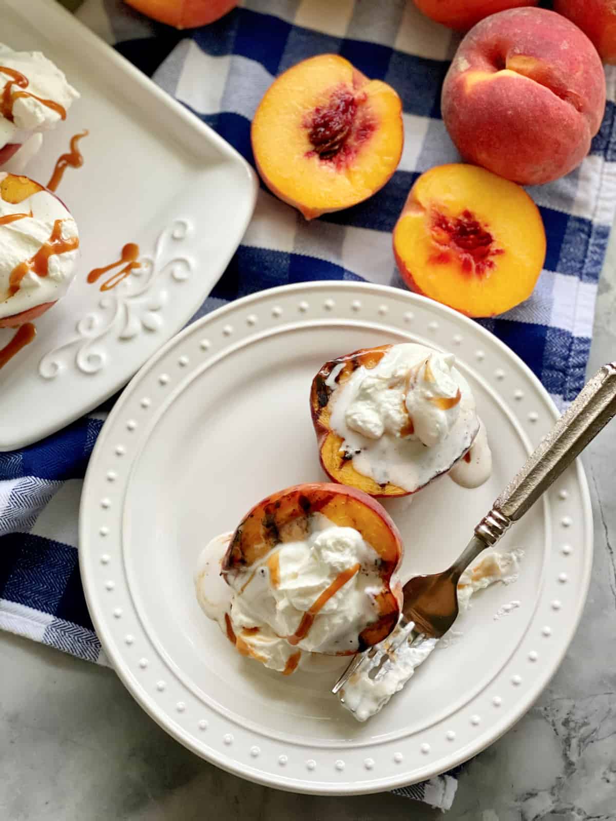 Top view of two grilled peaches on a white plate topped with whipped cream and caramel sauce.