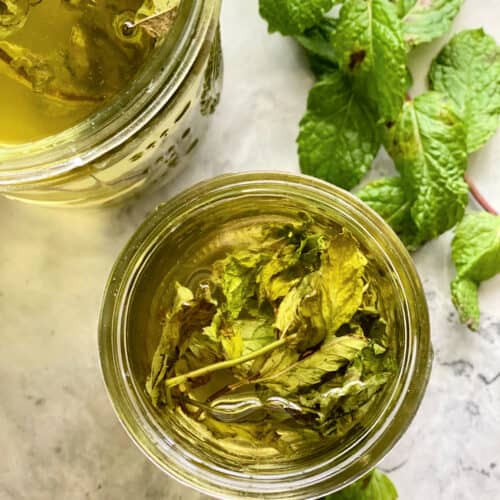 Top view of a glass jar filled with mint sprigs with clear liquid.