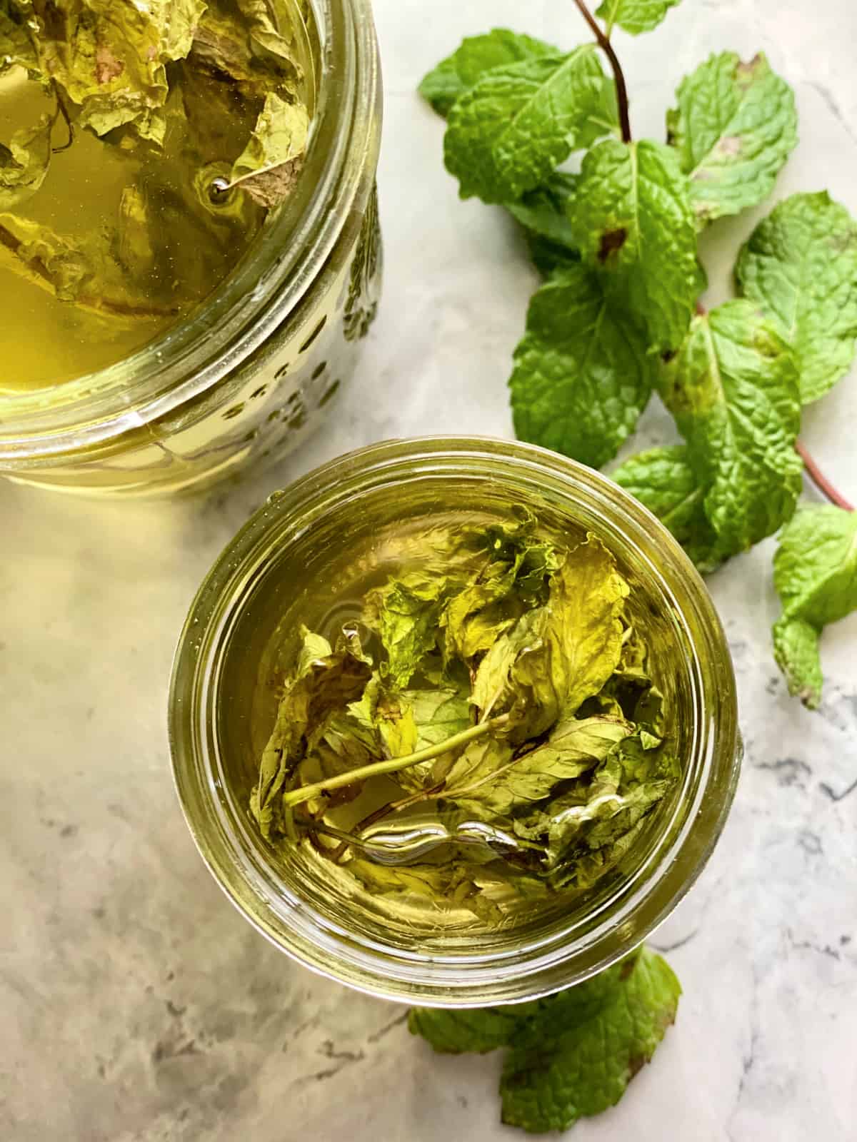 Top view of a glass jar filled with mint sprigs with clear liquid.