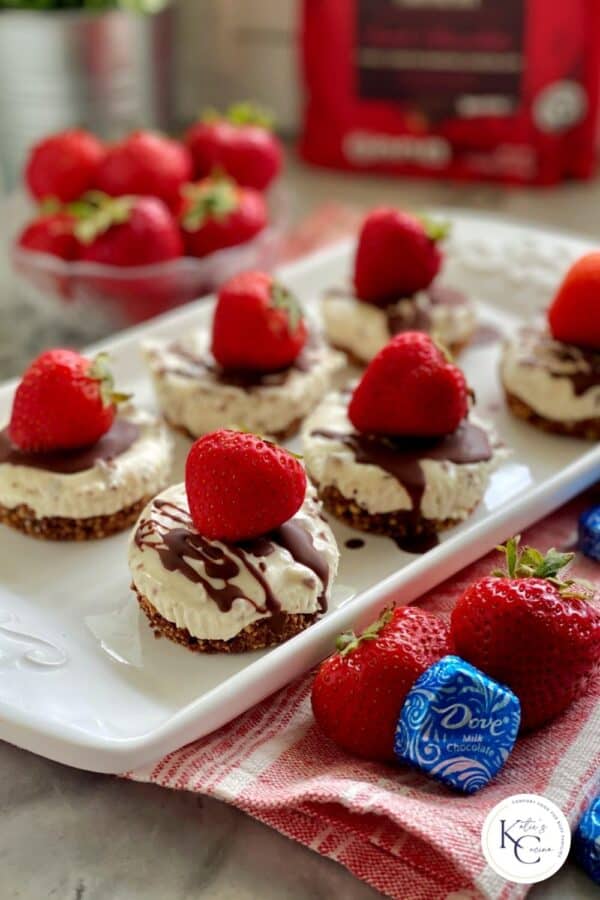 Platter of mini cheesecakes with drizzled chocolate and strawberries.