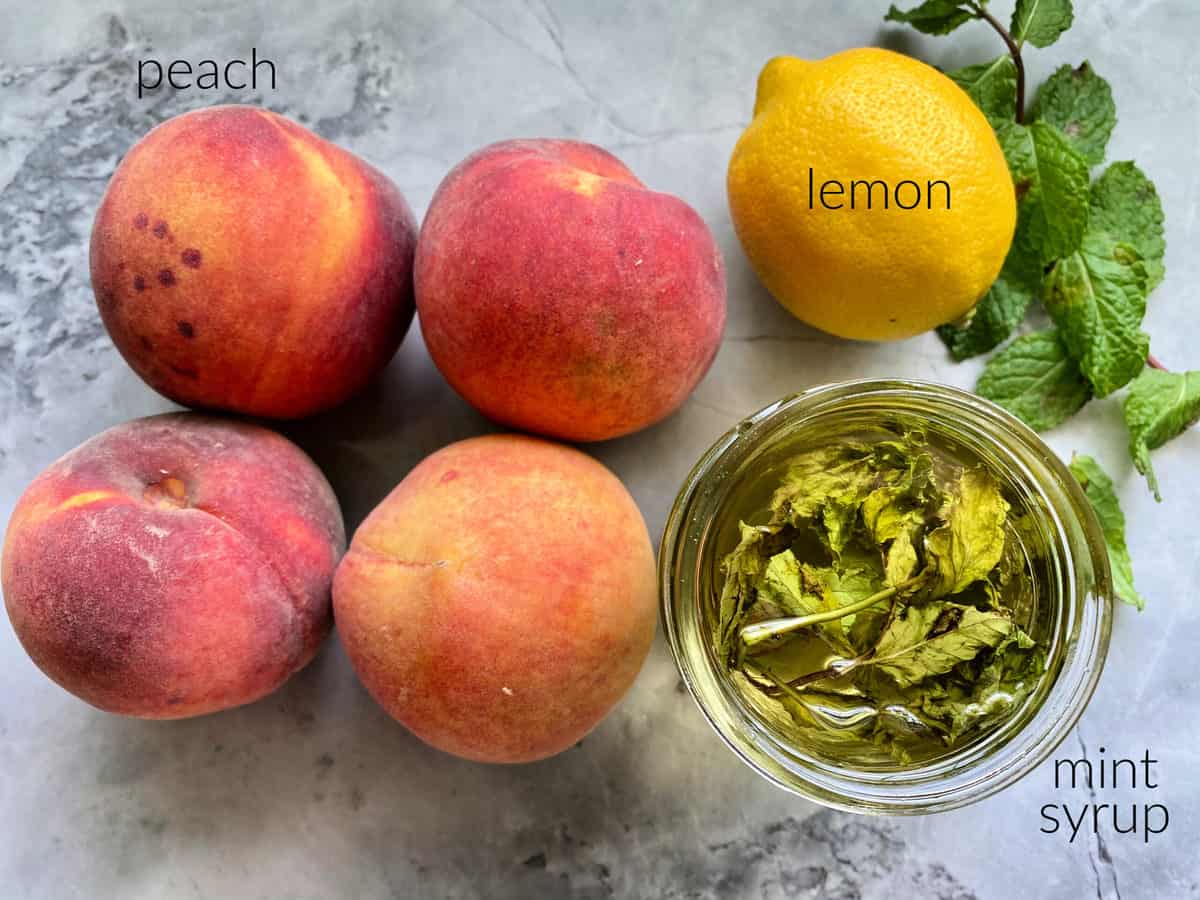 Ingredients on marble counter: peaches, lemon, mint syrup.