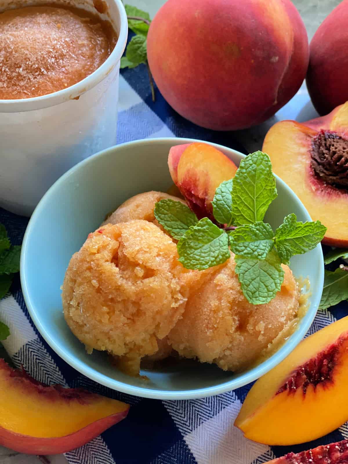 Blue bowl filled with scoops of Peach Mint Sorbet with fresh peaches and a pint of sorbet.