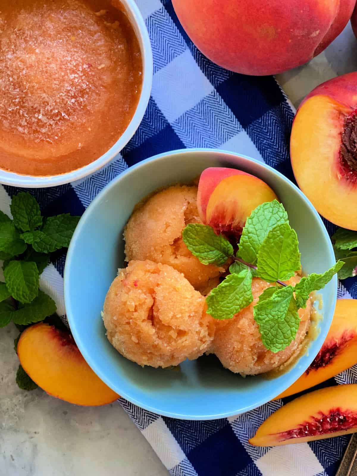 Top view of a bowl filled with scoops of sorbet with a pint of sorbet and fresh peaches around the bowl.