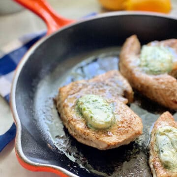 Orange cast iron skillet with 3 Swordfish Steaks with butter on top.