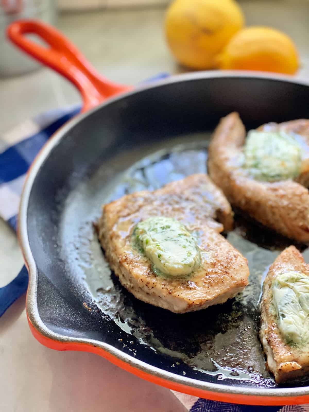 Orange cast iron skillet with 3 Swordfish Steaks with butter on top.