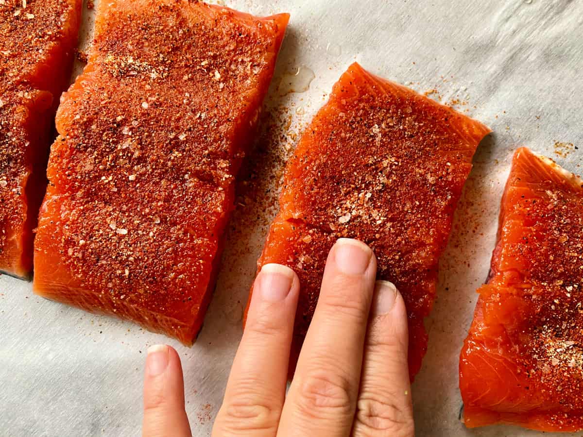 Top view of female hand rubbing seasoning on salmon filets.