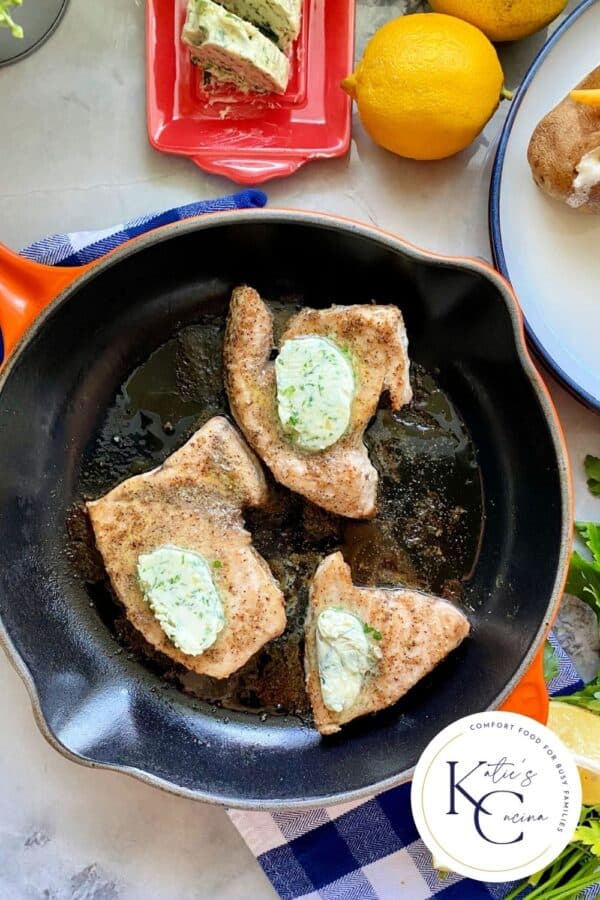 Top view of an orange cast iron skillet filled with 3 swordfish steaks topped with herb butter with logo on the right corner.