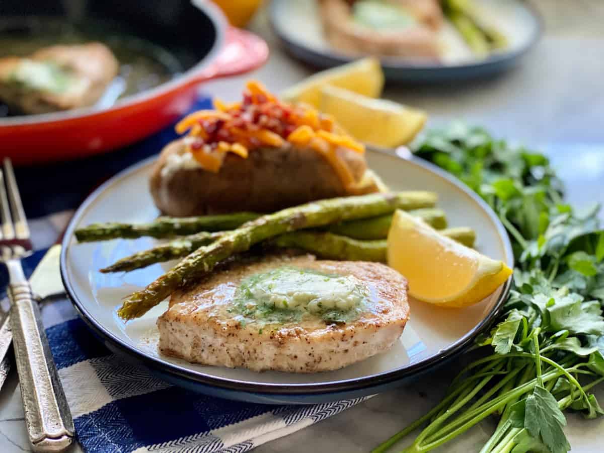 Round plate with Swordfish Steak wedge of lemon, asparagus spears and loaded baked potato.