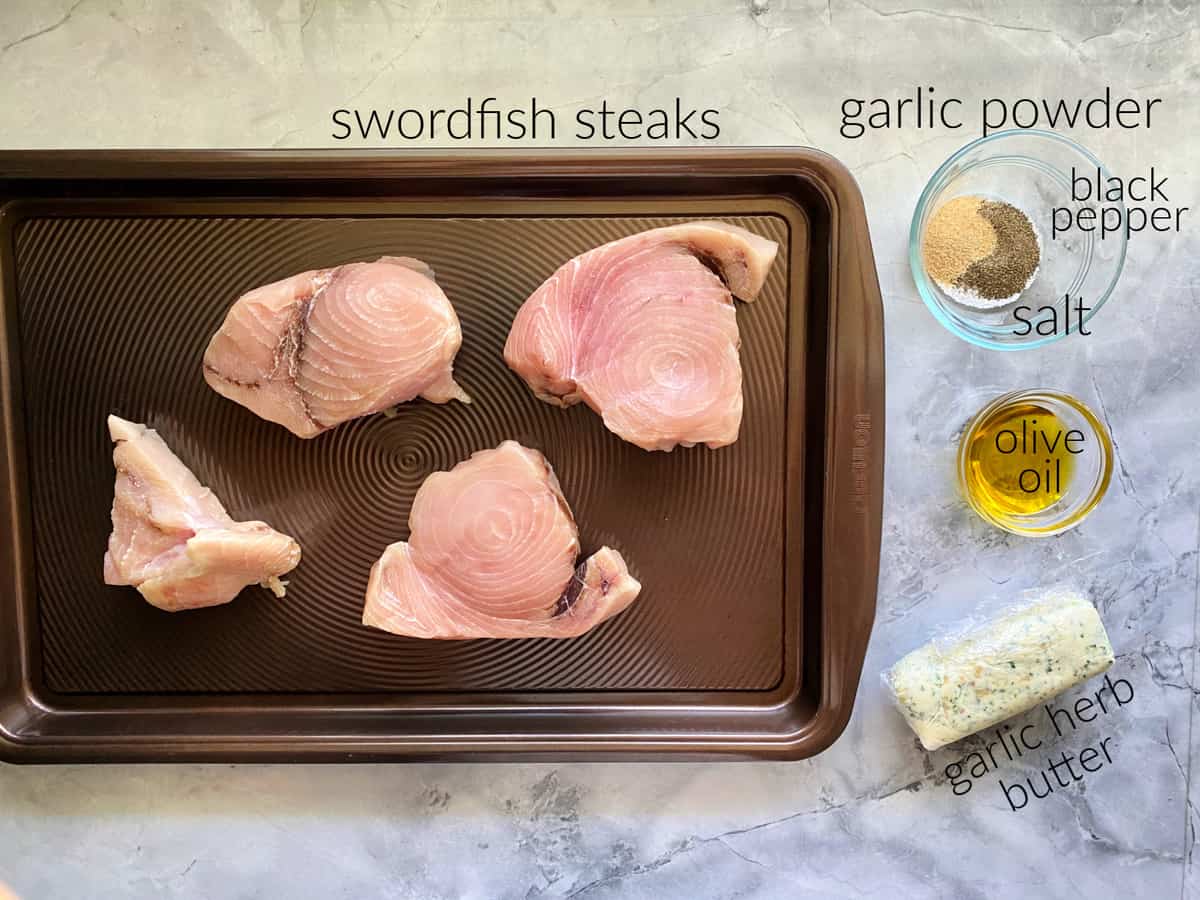 Ingredients; 4 swordfish steaks on a brown baking tray, garlic powder, black pepper, saalt, olive oil, and garli herb butter.