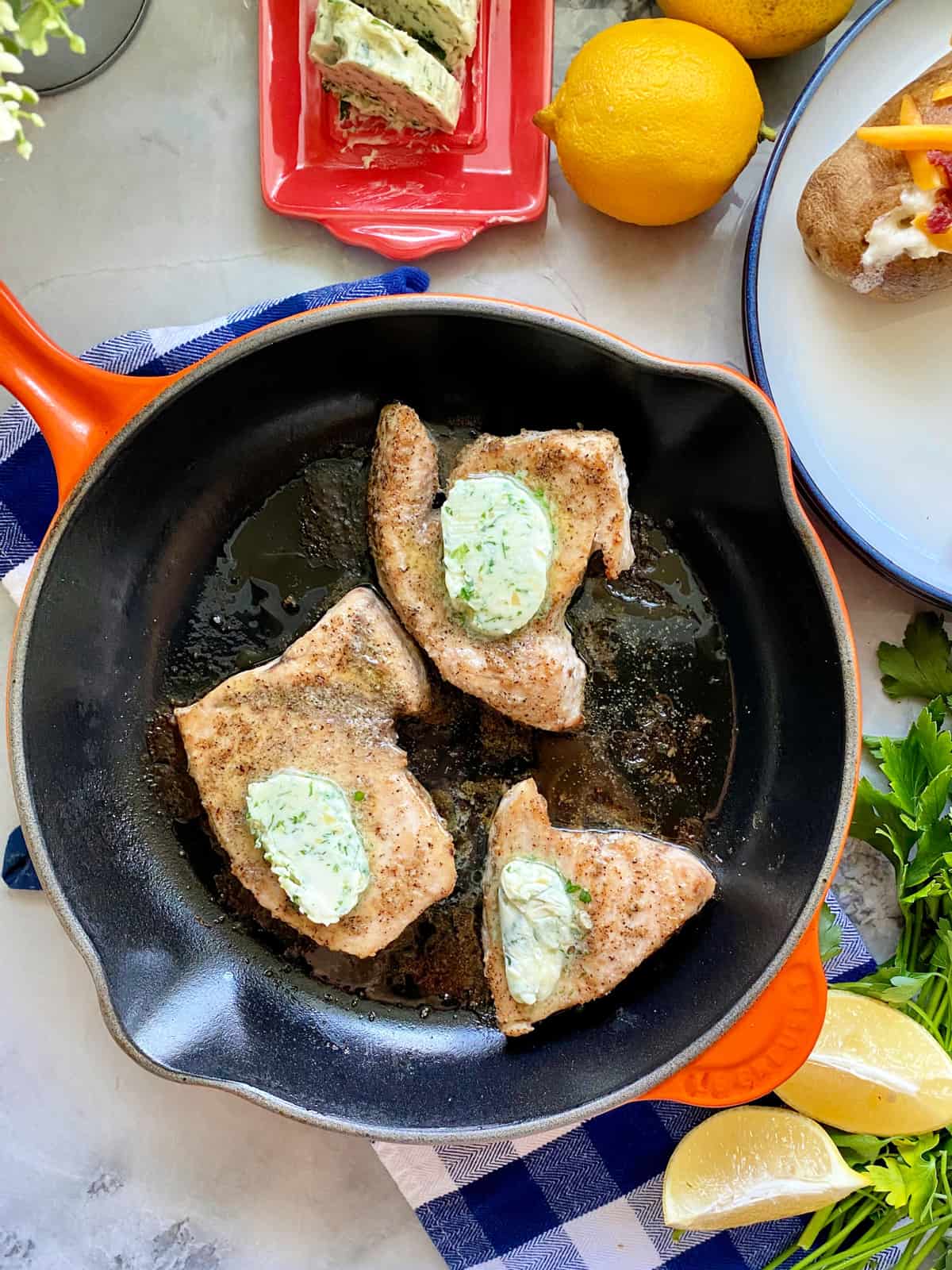 Top view of an orange cast iron skillet filled with three Swordfish Steaks topped with herb butter.