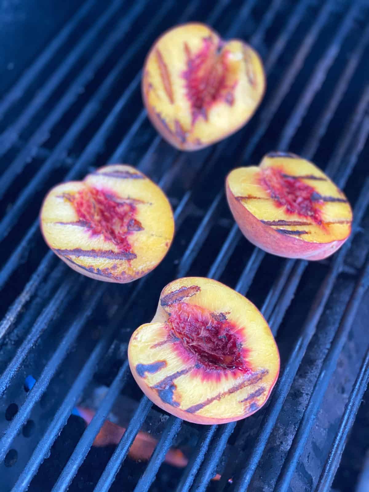 Four peaches with grill marks on grill grates with fire underneath them.