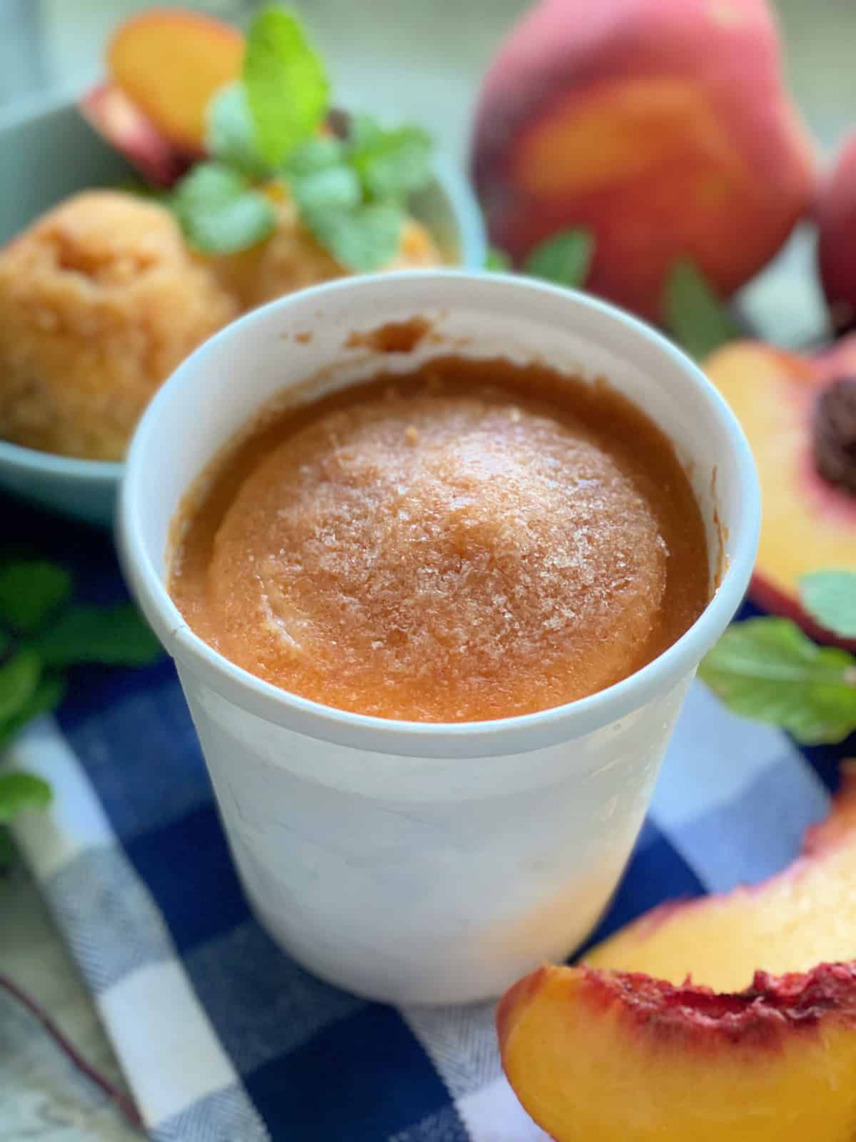 White pint container filled with peach sorbet with peaches in the background.