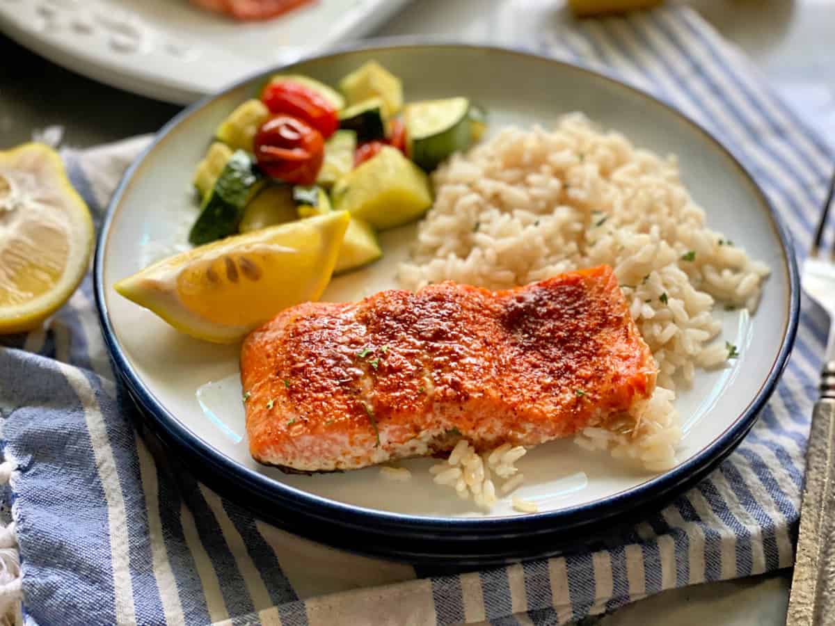 White plate filled with salmon filet, lemon wedge, white rice, and zucchini.