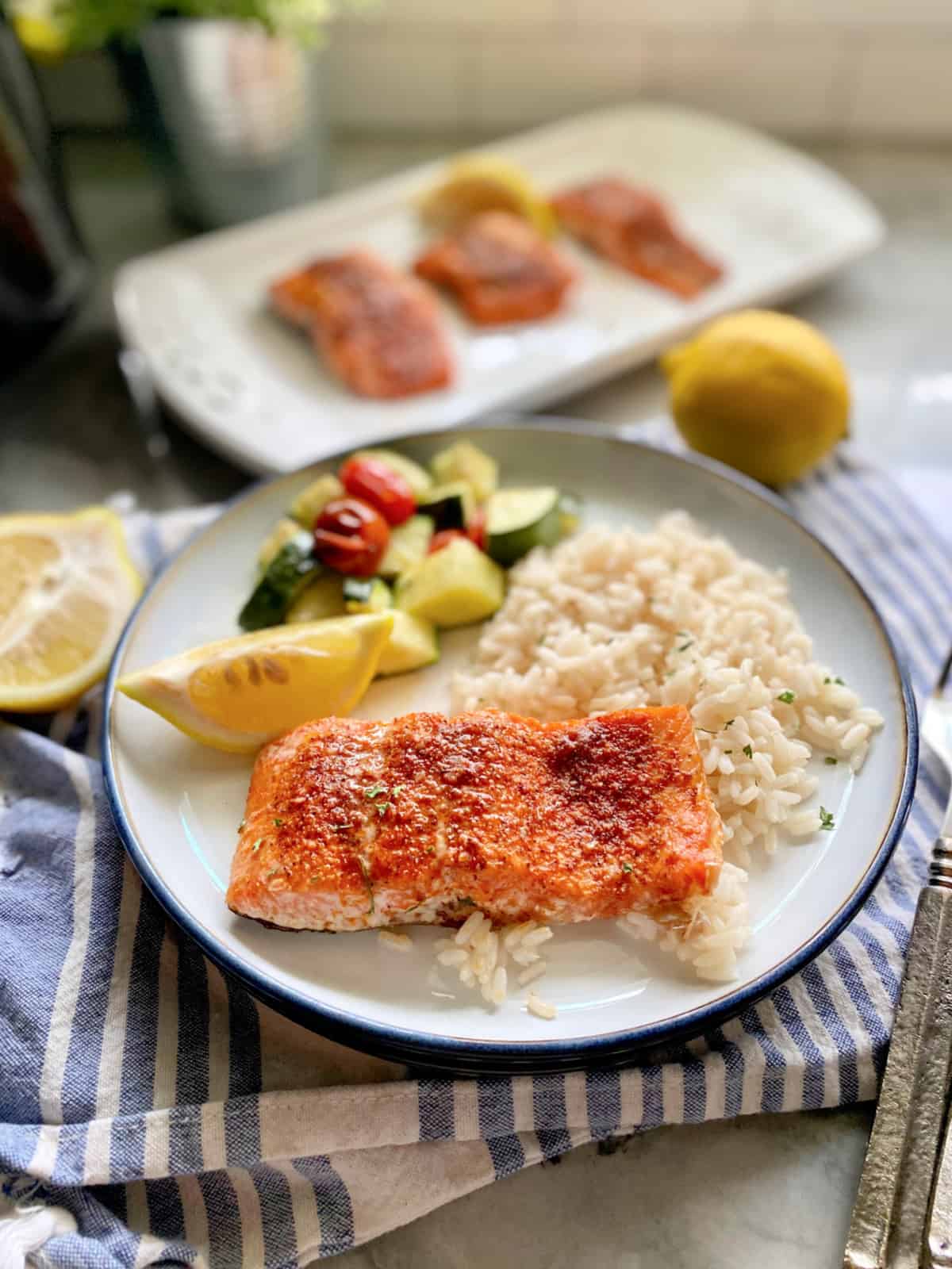 White plate filled with salmon, rice, and salmon filets on platter in background.